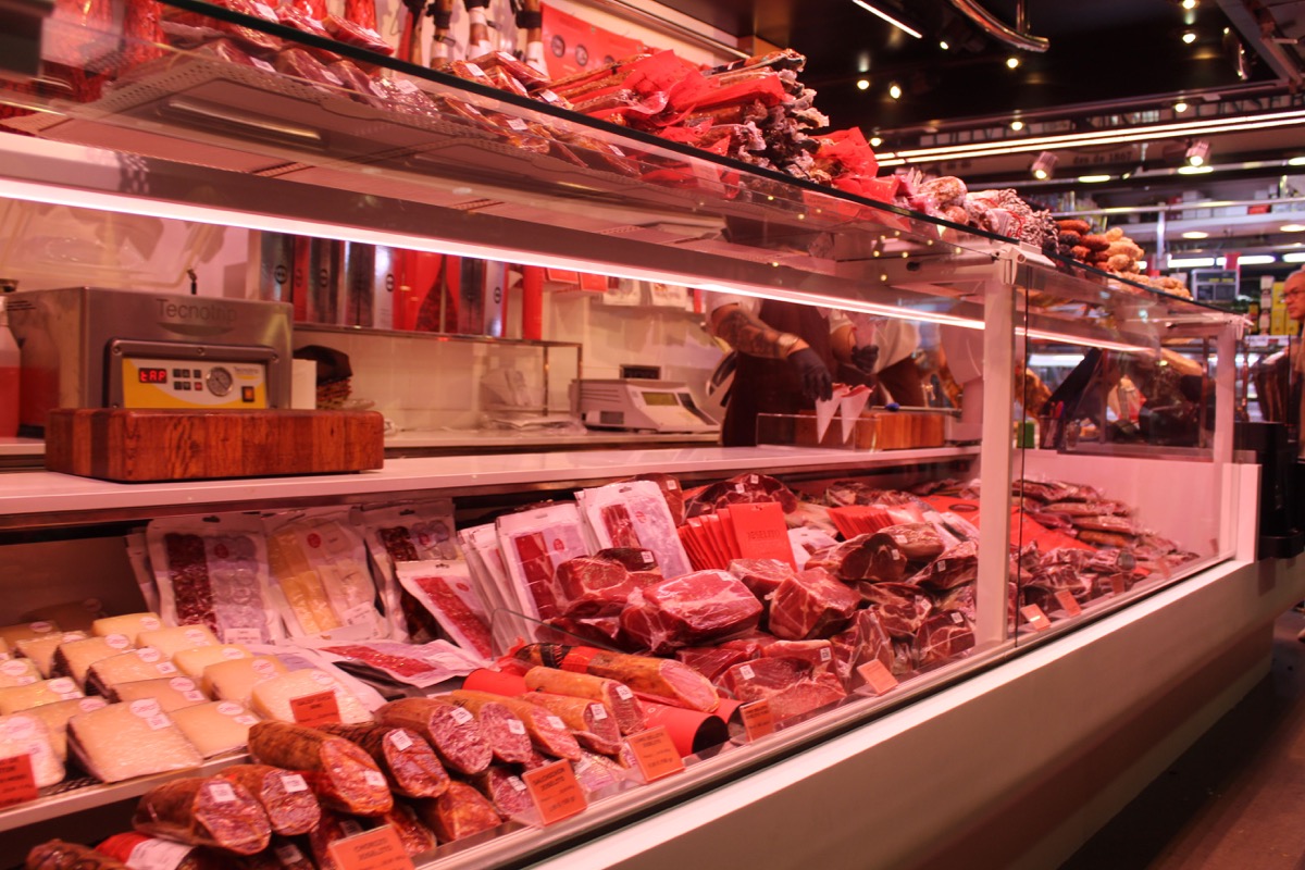 Shopper view of a supermarket meat and deli counter with packaged cuts and labels behind glass